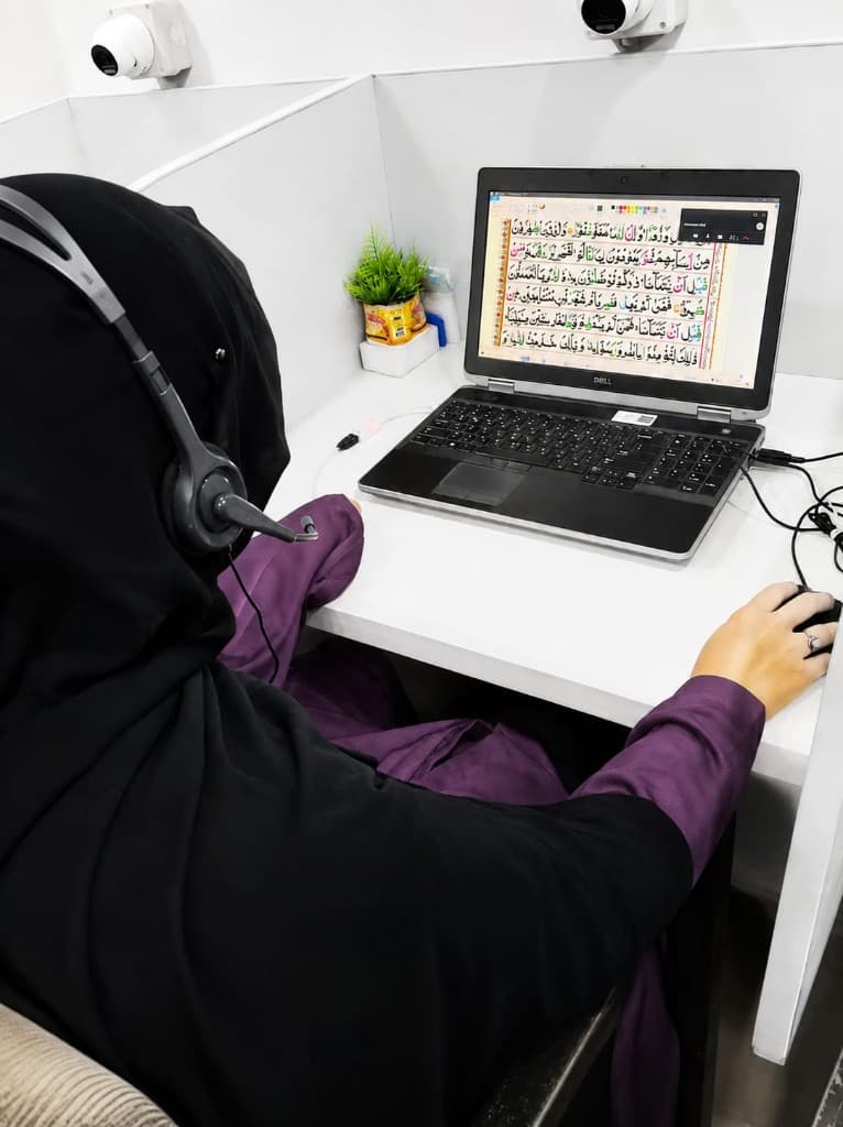 Teacher guiding a live online Tajweed lesson with the Quran on screen